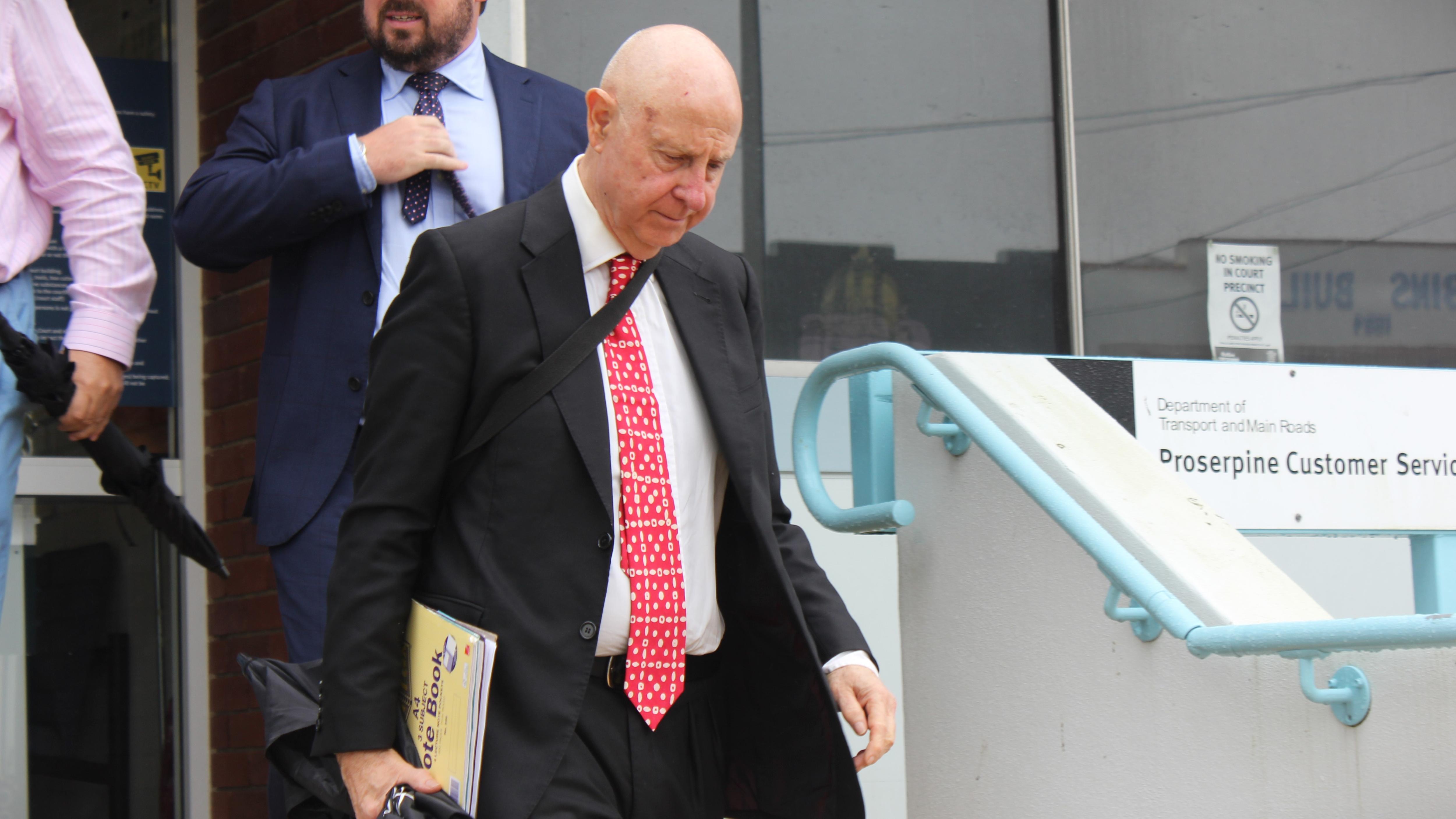 Older man in suit with red tie leaving court house 