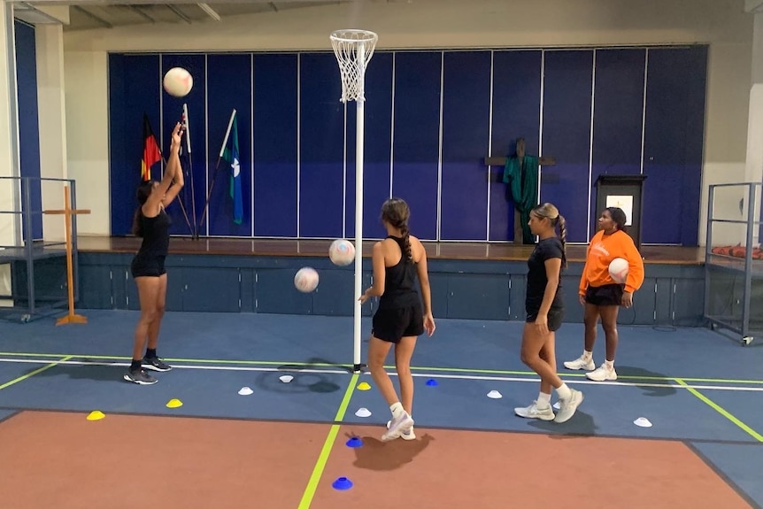 Three young female netballers stand on a training court, practicing shooting goals.