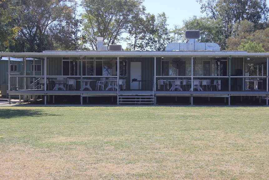 A demountable building with tables and chairs on the verandah, with grass in front of it.