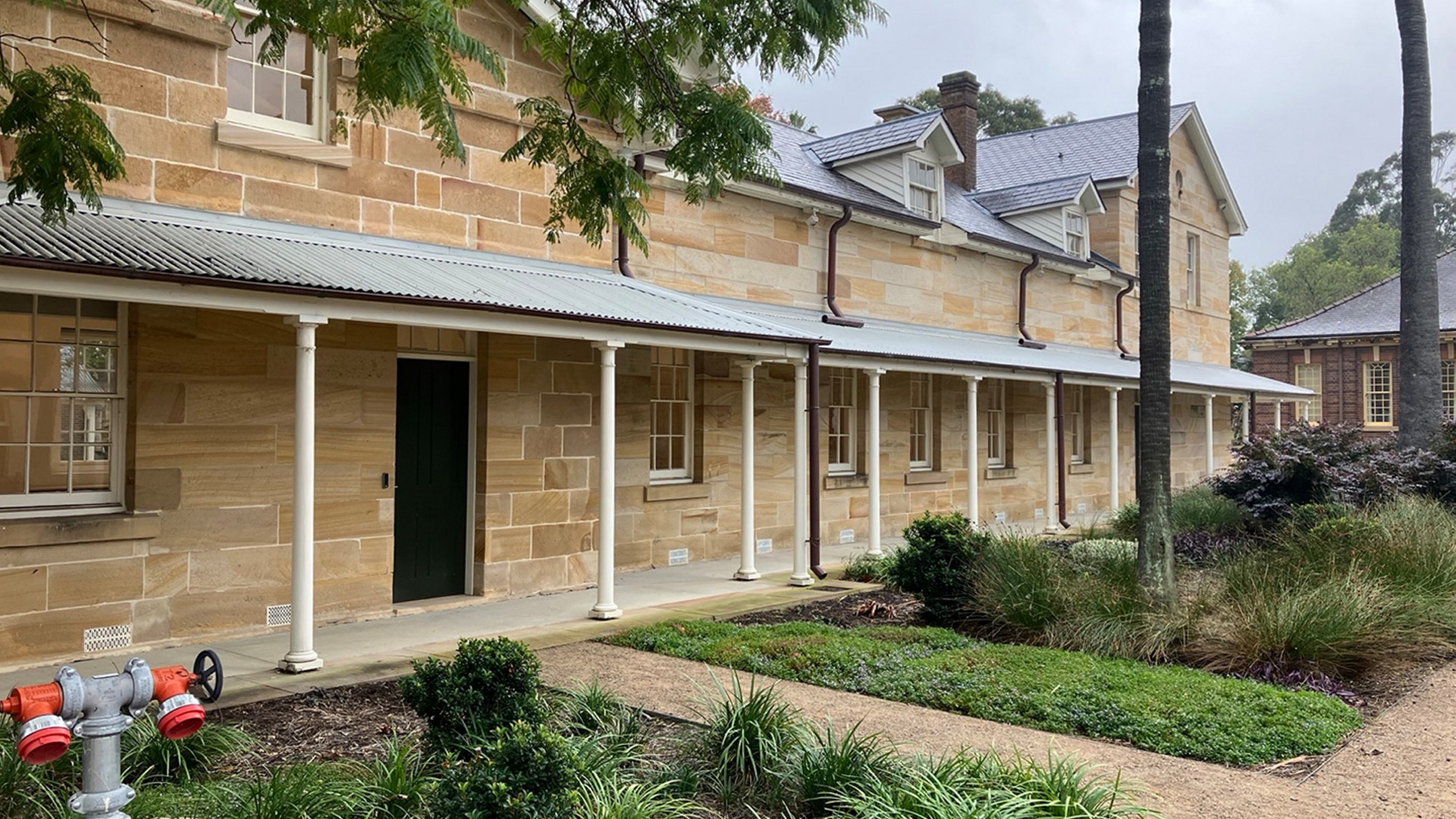 Exterior of sandstone building with white pillars and greenery