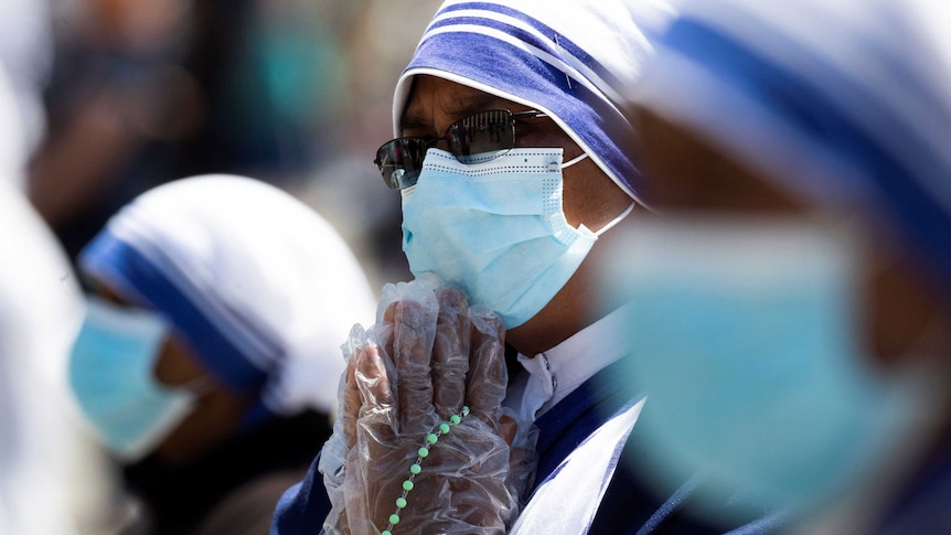 Nuns wearing gloves and protective facemask pray in Saint Peter's Square at the Vatican