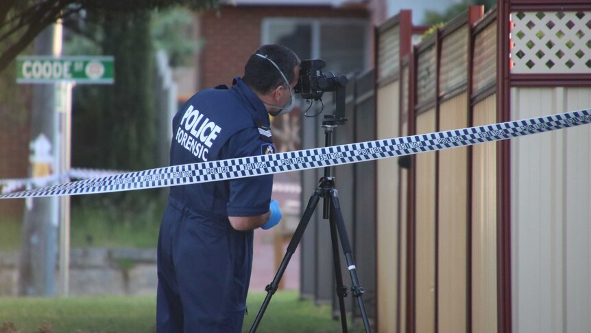 A WA Police forensic officer stands behind a camera on a tripod outside a house in Bedford.