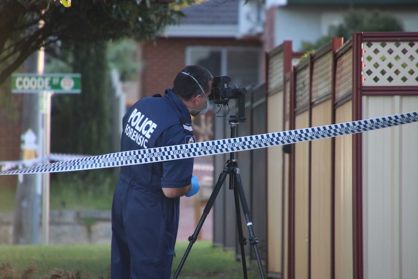 A WA Police forensic officer stands behind a camera on a tripod outside a house in Bedford.