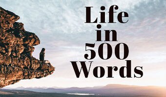 A person on a rocky out crop looking at a sunrise with words "Life in 500 Words" over the clouds