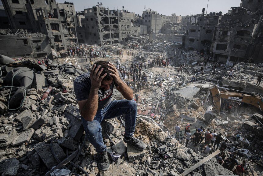 A man sits amongst rubble, his head in his hands.