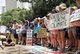 Students stand holding signs at the front of a large rally calling for action on climate change.