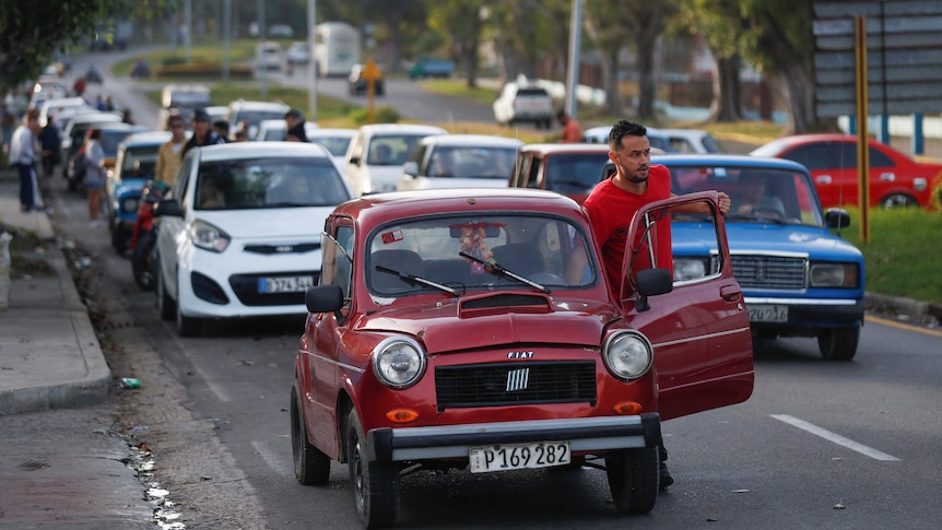 A man pushes his small red car while waiting to fill up at a Cuba petrol station