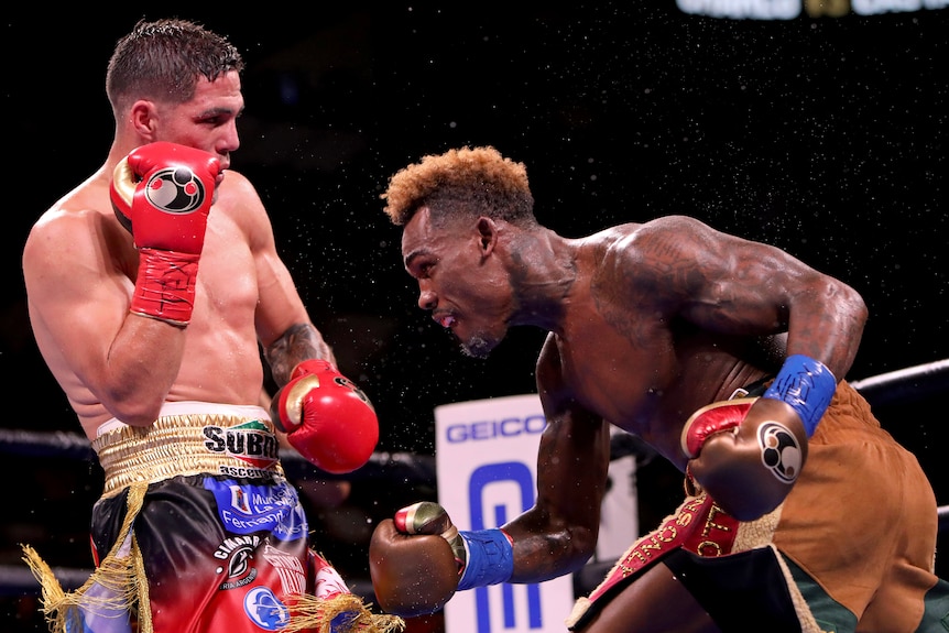 Jermell Charlo bends forward and Brian Castano stands upright in a boxing ring