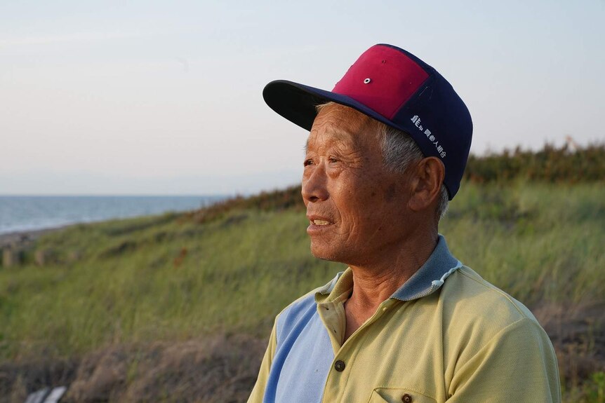 An elderly Japanese man on a beach looks across to the sea.