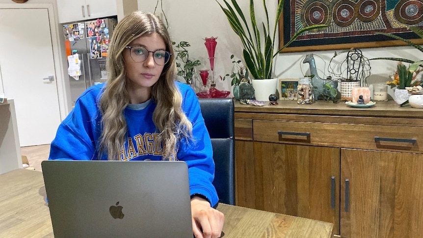 A young woman in a blue jumper sitting in front of a laptop