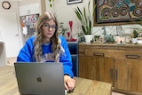 A young woman in a blue jumper sitting in front of a laptop