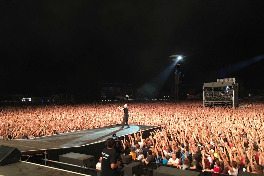 Peter Garrett on stage, crowd surrounds him with hands in the air