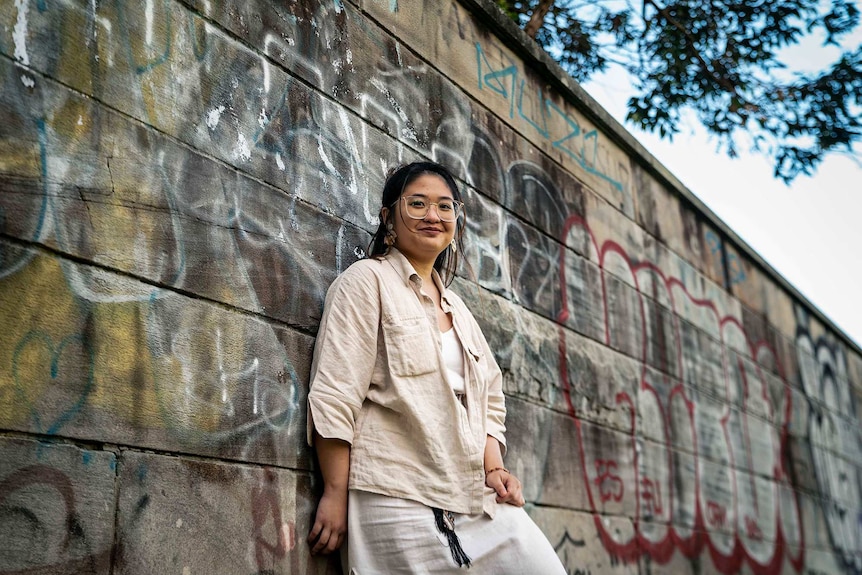 Rosario leaning against a wall with graffiti on it.