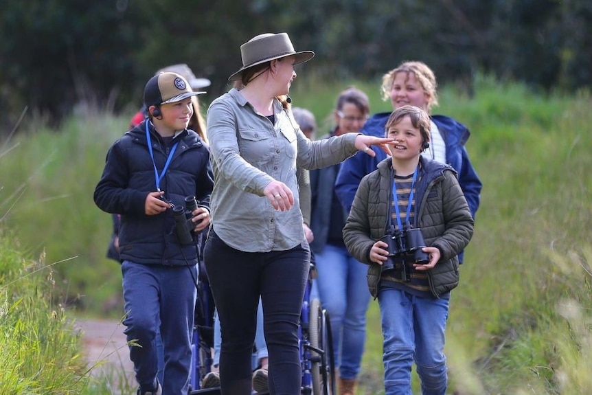 a tour guide points to a child in a group walking through grassland