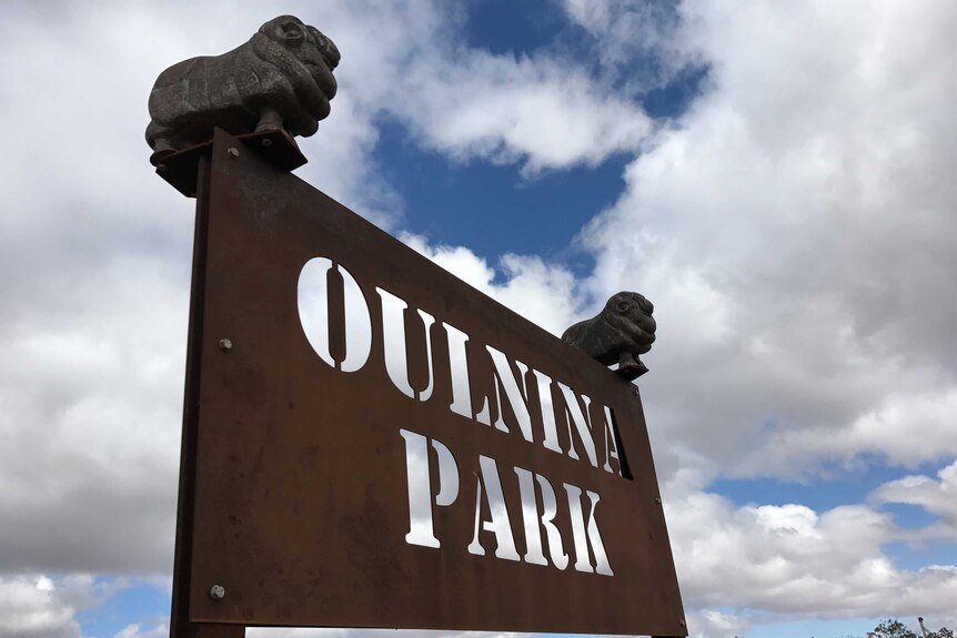 A rusted sign that reads Oulnina Station that has two sheep statues on the top corners