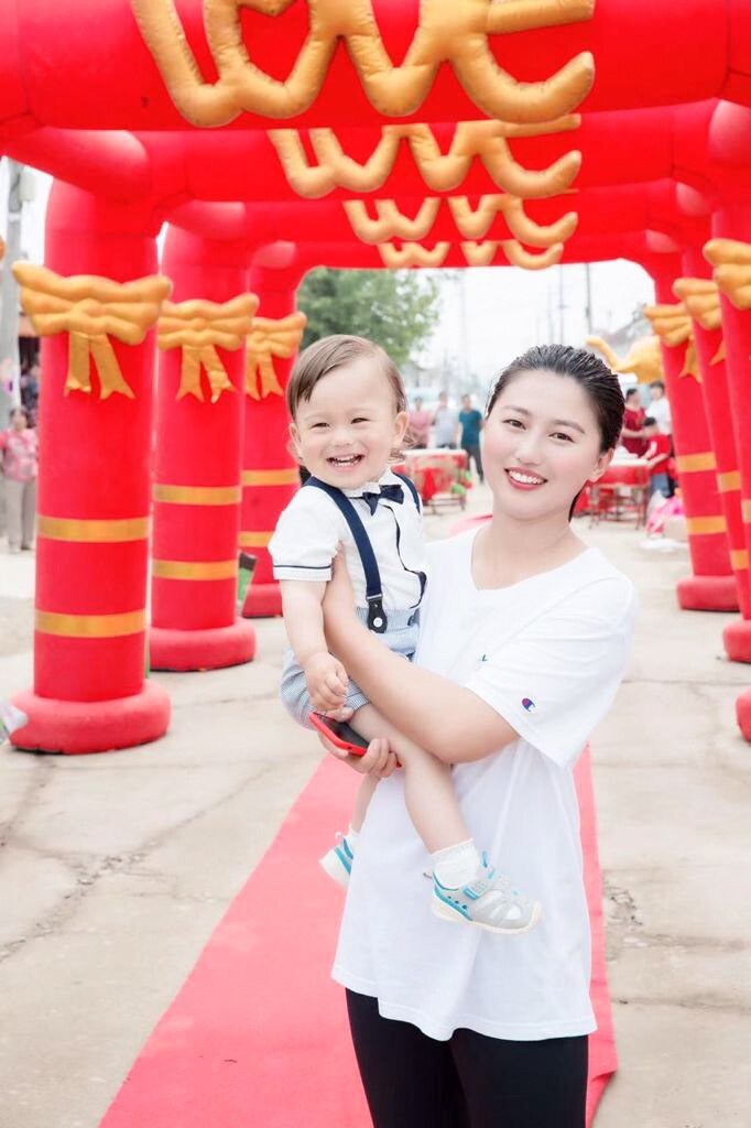 A woman smiles as she holds a baby boy wearing suspenders and a bow tie.
