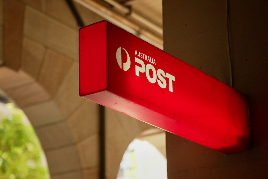 Close-up of Australia Post sign in a cream brick building with two arches visible.