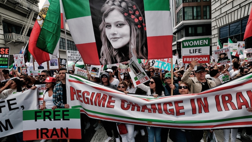 People hold green, white and red signs that say free Iran and a large photo of Mahsa Amini. 