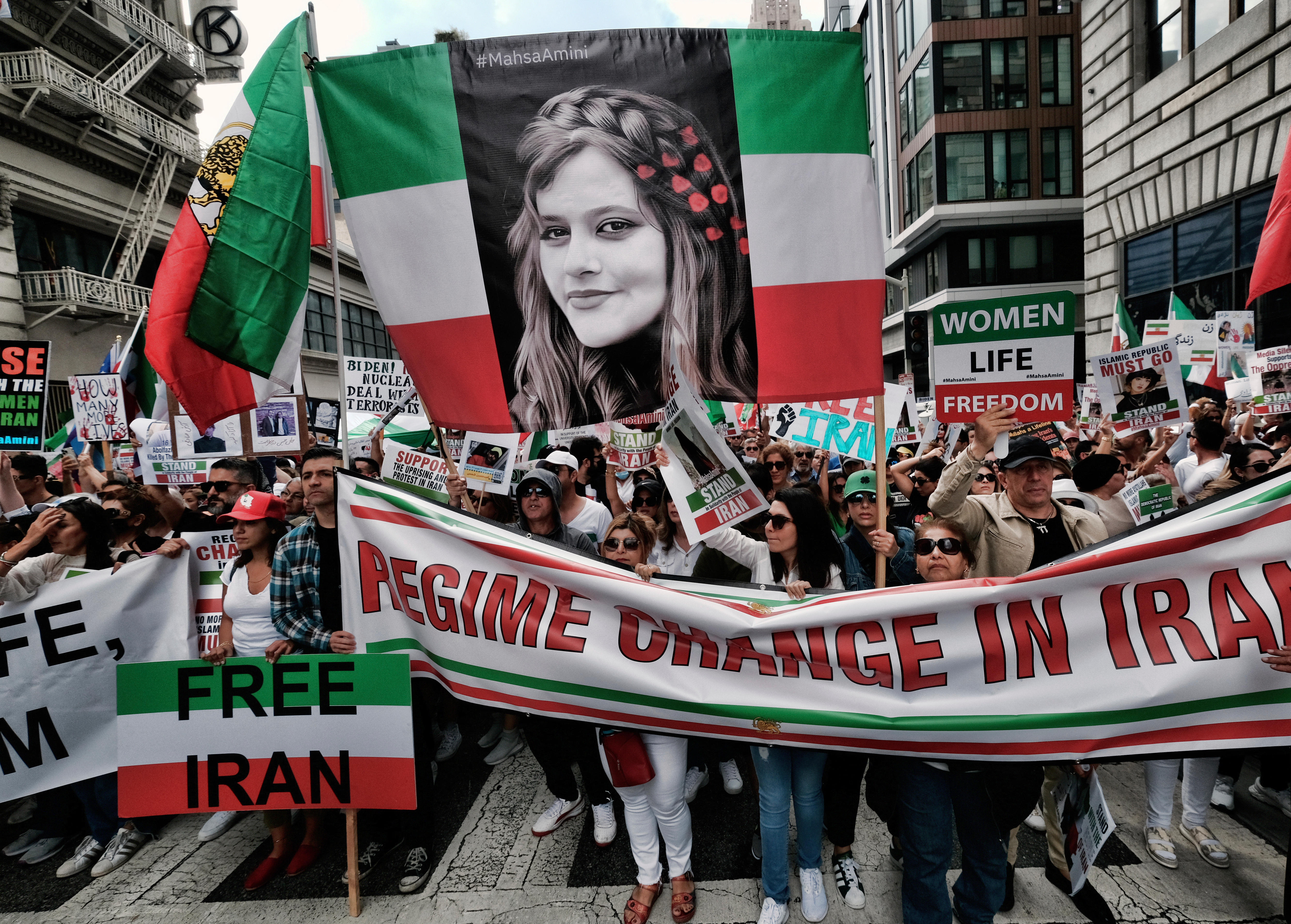 人们举着绿色、白色和红色的标语，上面写着自由伊朗和 Mahsa Amini 的大幅照片。 