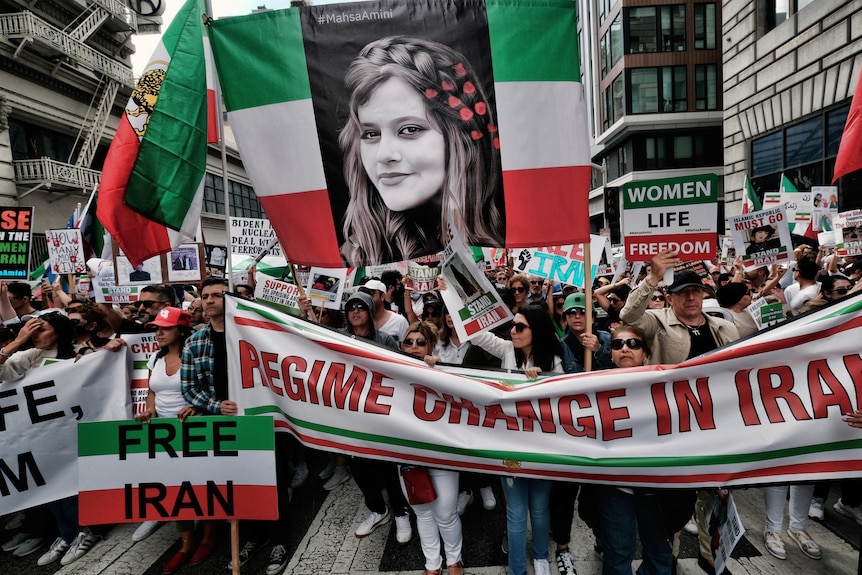 People hold green, white and red signs that say free Iran and a large photo of Mahsa Amini. 