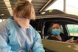 A woman hands over a medicare card to a nurse in PPE at a drive-through vaccination clinic.