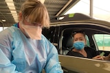 A woman hands over a medicare card to a nurse in PPE at a drive-through vaccination clinic.