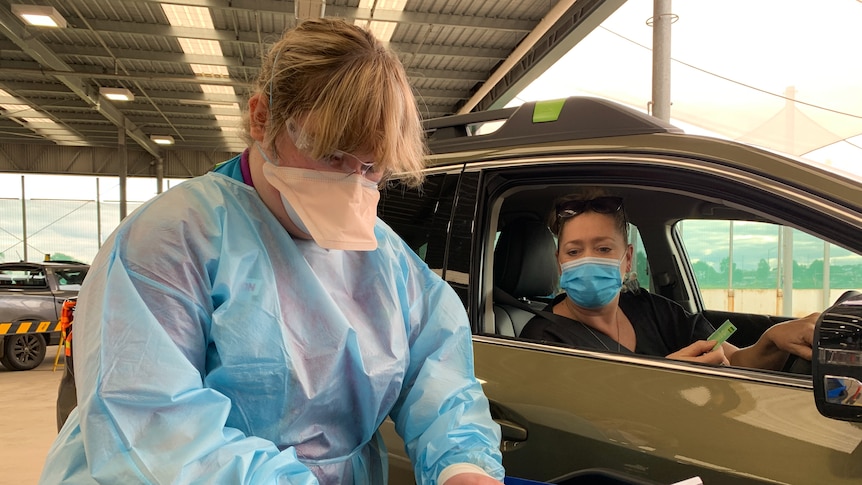 A woman hands over a medicare card to a nurse in PPE at a drive-through vaccination clinic.