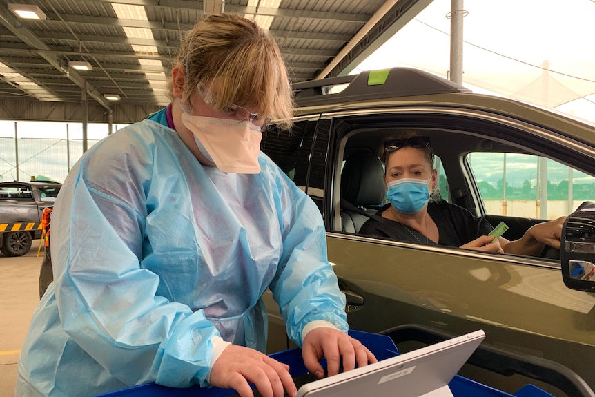 A woman hands over a medicare card to a nurse in PPE at a drive-through vaccination clinic.