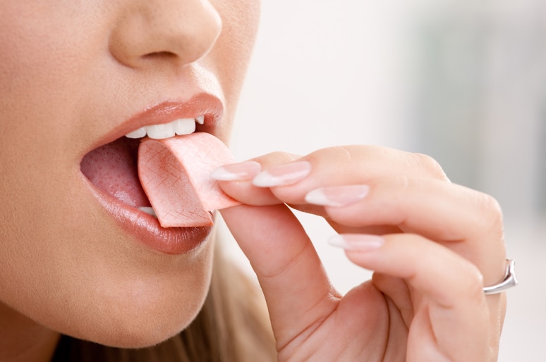A woman putting a piece of chewing gum into her mouth.