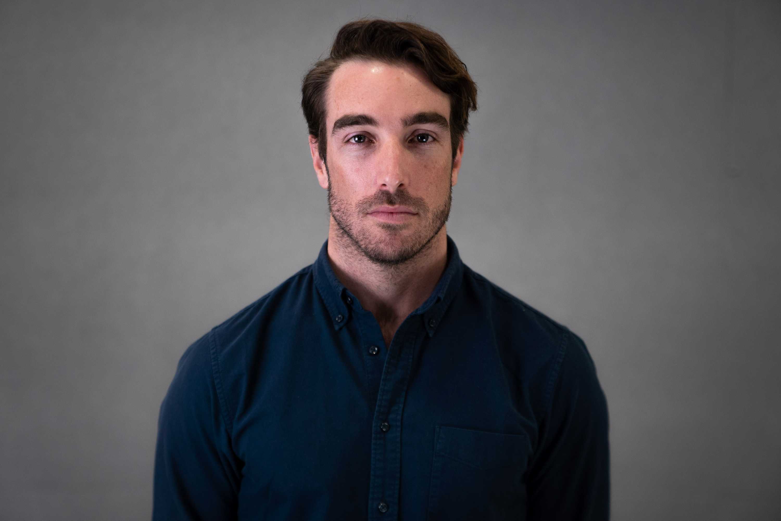 Sean Rubinsztein-Dunlop wearing blue collared shirt stands in front of grey background