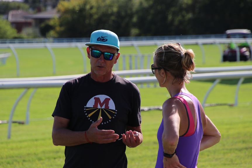 Nic Bideau stands in a black t-shirt talking to a female runner