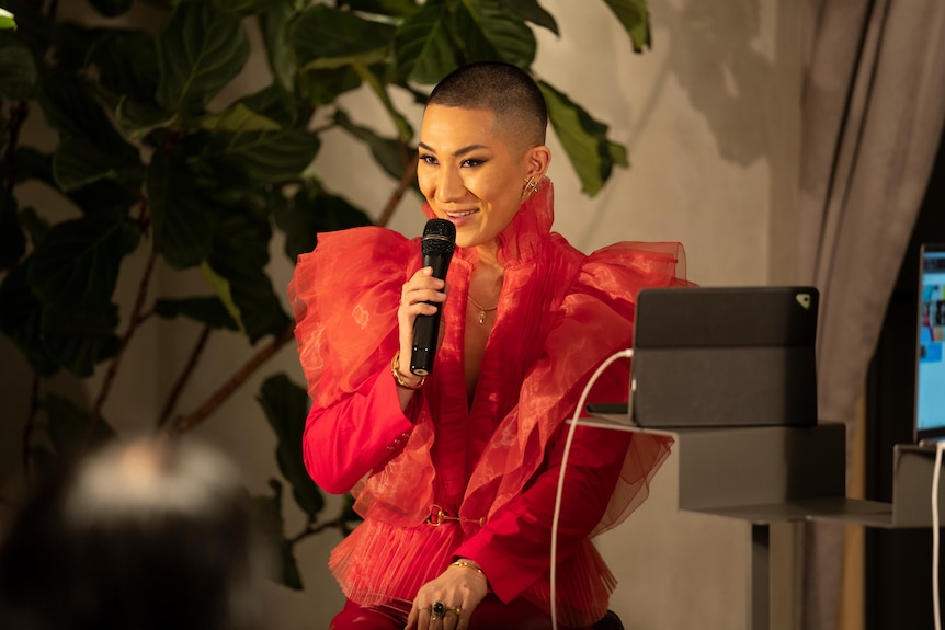 A man in a hot pink ruffled jacket holding a microphone