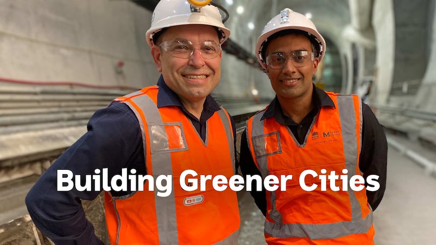 Two men wearing hard hats, high vis construction worker jackets, smiling at the camera in a tunnel construction site