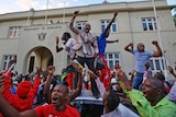Zimbabweans stand on a car and wave their arms in celebration.
