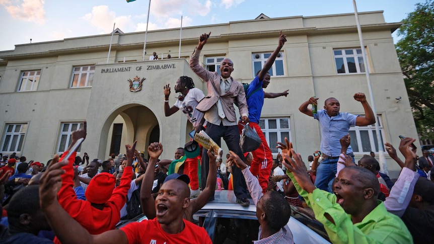 Zimbabweans stand on a car and wave their arms in celebration.