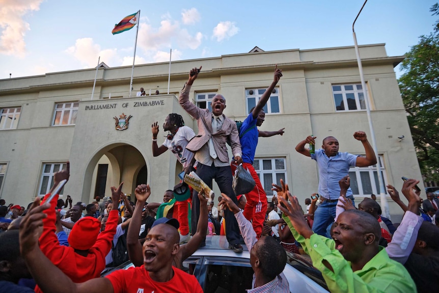 Zimbabweans stand on a car and wave their arms in celebration.