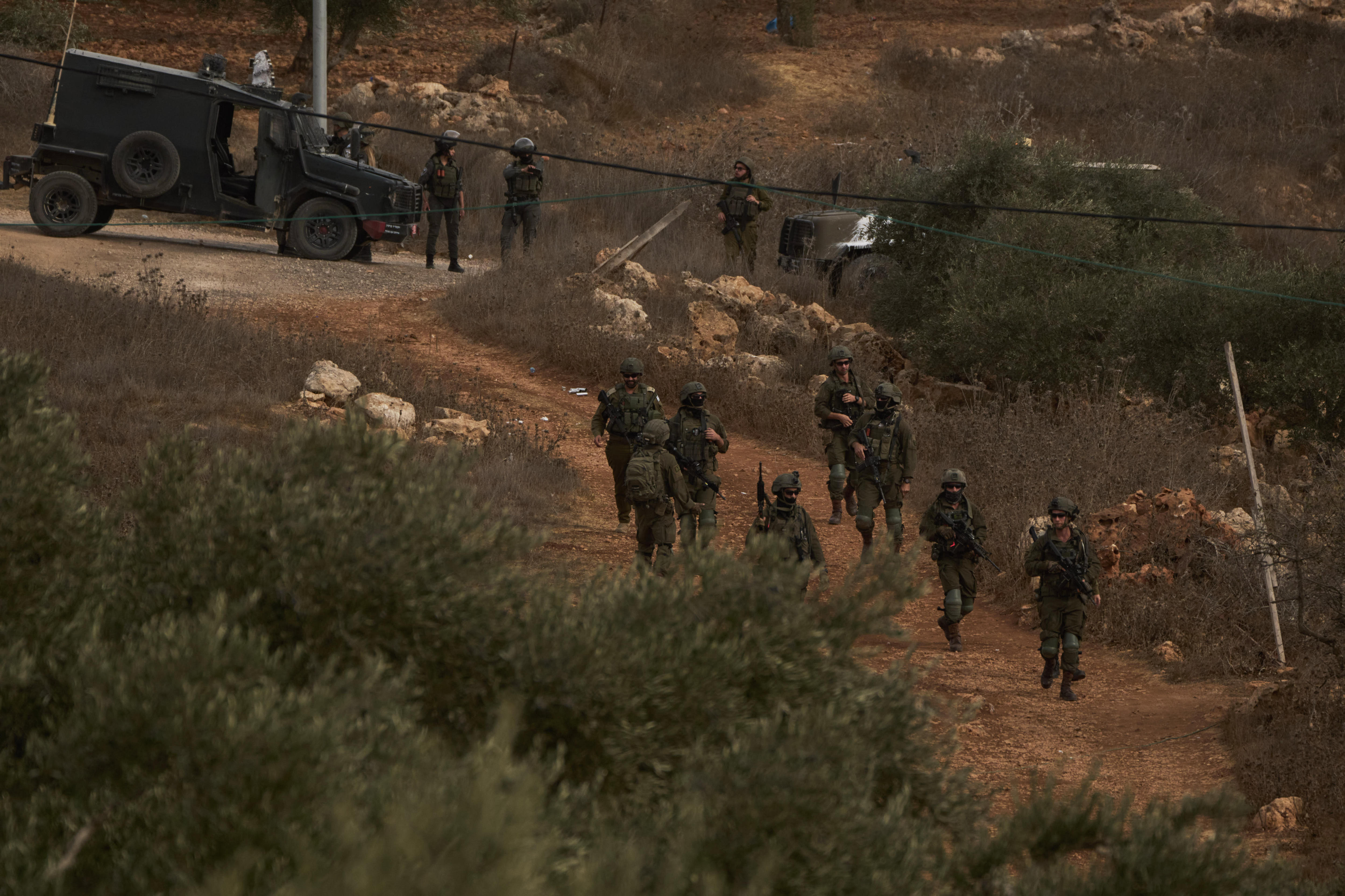 Several officers in army uniforms walk through an olive grove