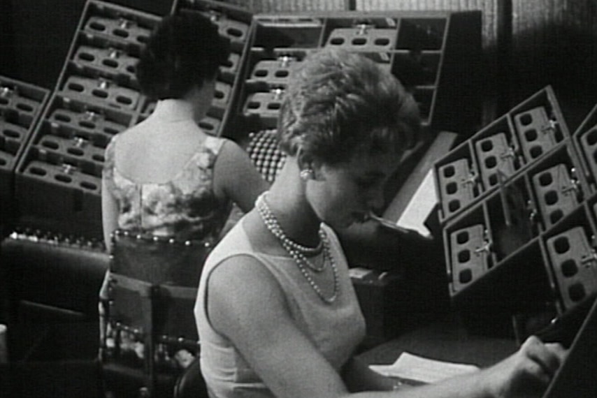 Black and white still of two women operating mechanical counters.