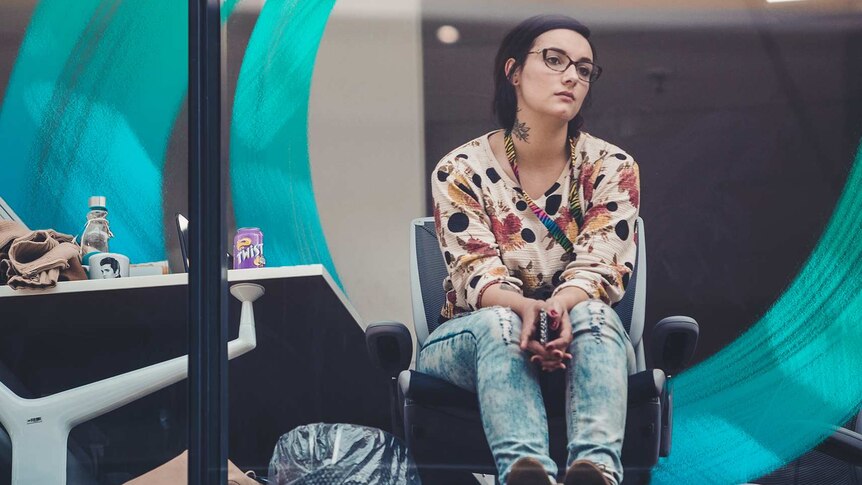Woman gazing out of office window looking bored and forlorn in a story about why we procrastinate and how to avoid it.
