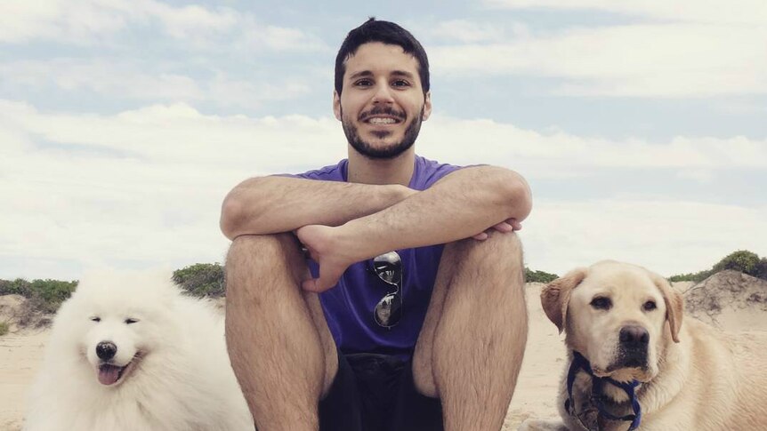 Pat Seyrak sits on a beach with two dogs.