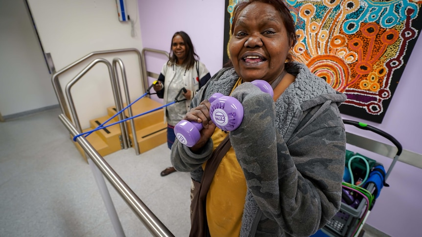 Two young women in an exercise class in central Australia. One holds purple hand weights, the other a resistance band.