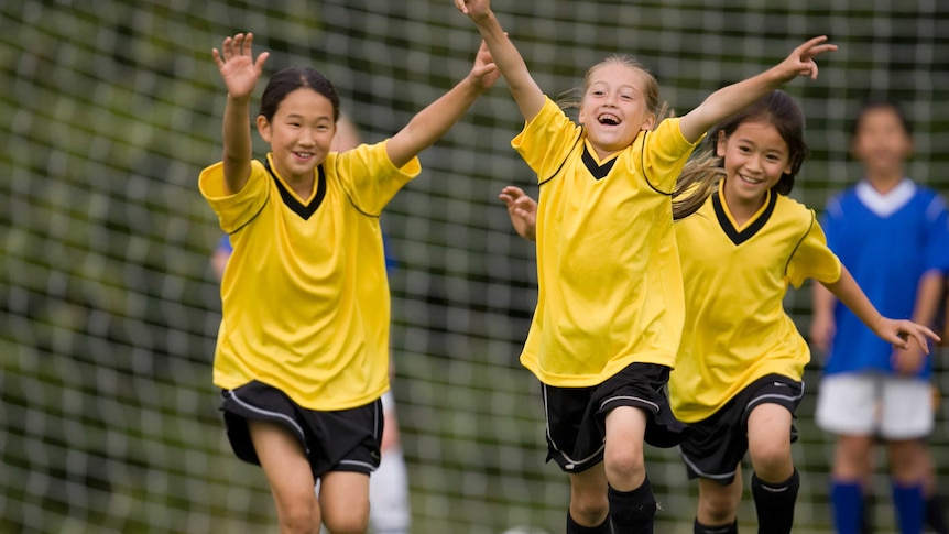 Three young girls wearing yellow soccer jerseys celebrate after scoring a goal