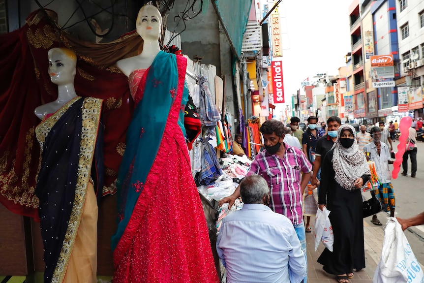 Une femme portant une burqa passe devant un marché de vêtements et de textiles très fréquenté le long d'une rue commerçante principale.