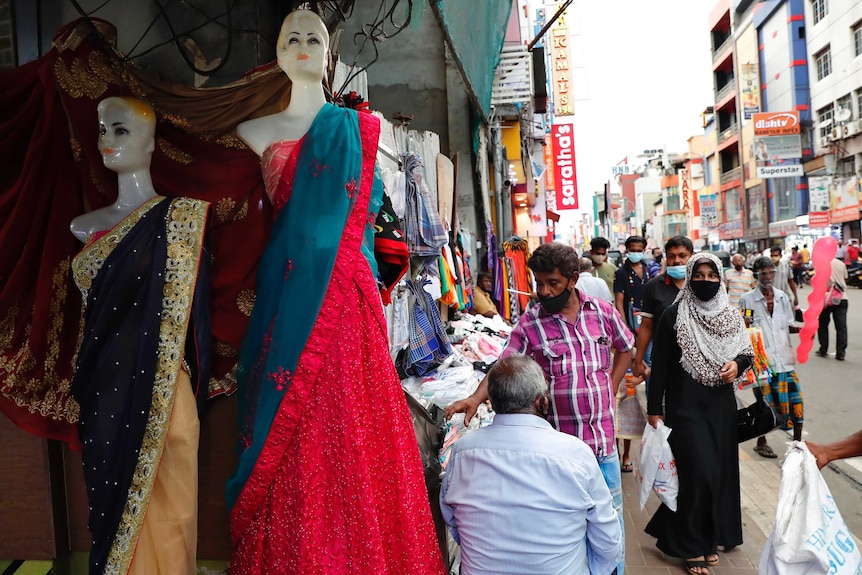 A woman wearing a burqa walks past a busy garment and textile market along a main shopping road.