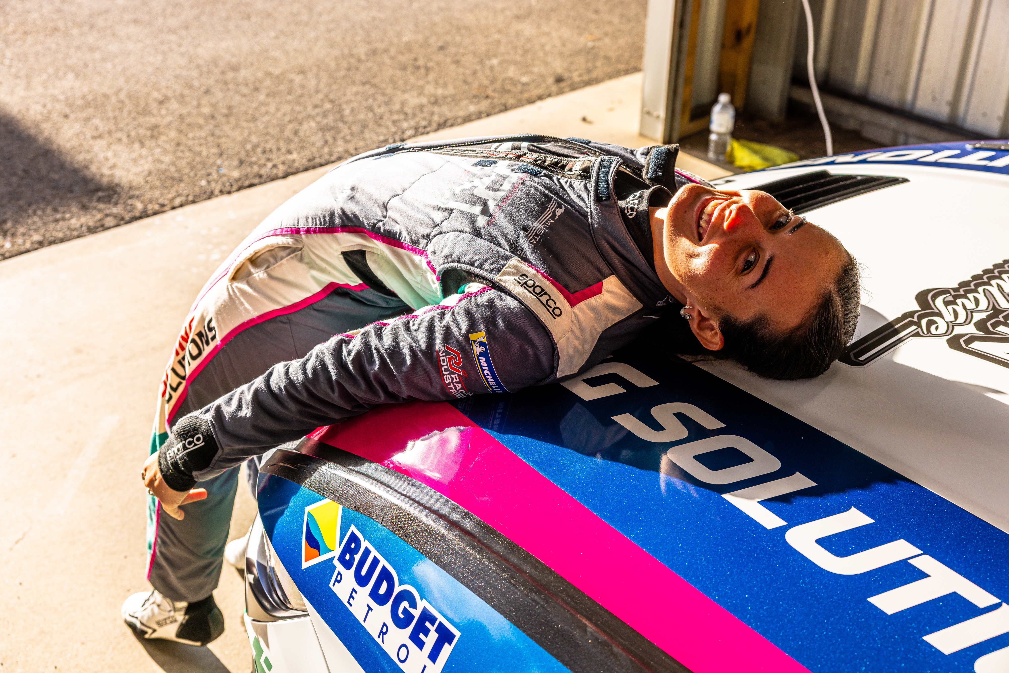 Imogen Radburn usa sua roupa de corrida e se apoia em seu carro na garagem. 