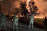 Law enforcement stand guard as a fire burns in a field in central Mexico.