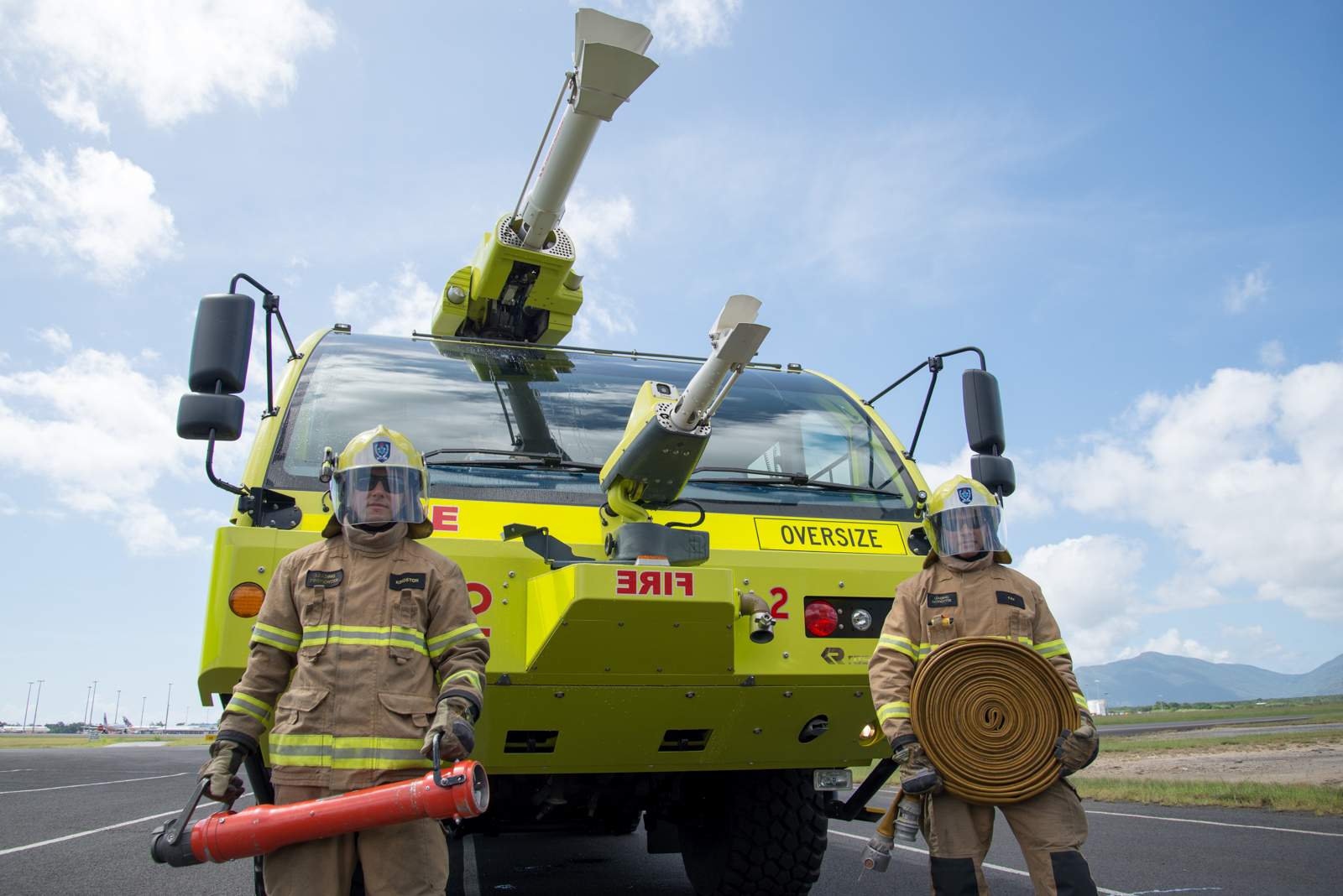 Two aviation firefighters stand in front of a specially designed, bright yellow fire truck.