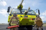 Two aviation firefighters stand in front of a specially designed, bright yellow fire truck.