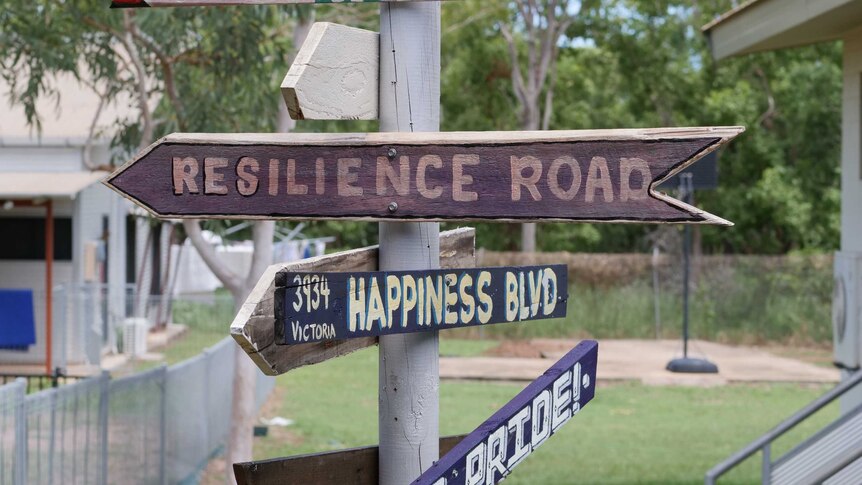 Wooden signs reading 'resilience road', 'happiness road' and 'pride' pointing in different directions and nailed to a post.