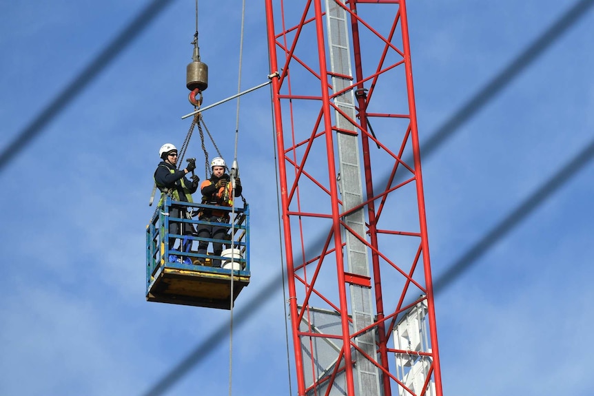 Workers in a metal basket suspended in the air work to dismantle the crane.